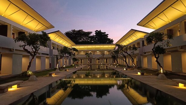 A modern hotel courtyard with a central pool, surrounded by trees and illuminated by warm lighting. - Kuta Living (Kuta)
