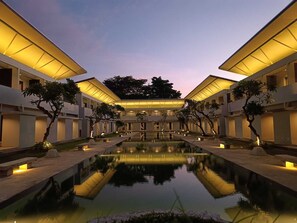 A modern hotel courtyard with a central pool, surrounded by trees and illuminated by warm lighting. - Kuta Living (Kuta)