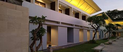 A modern building with multiple balconies, a well-maintained lawn, and a series of benches along the walkway.