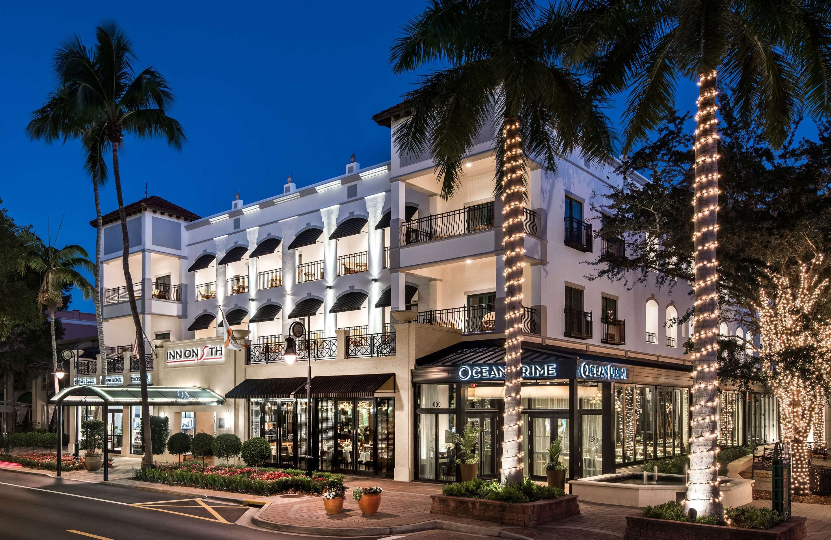 A multi-story hotel with balconies, palm trees, and storefronts including Ocean Prime.