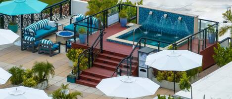 A rooftop pool area with a jacuzzi, outdoor seating, and a staircase leading to the pool.