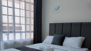 Een net opgemaakt bed met wit en donker beddengoed, een hoofdbord en een wekkerklok op het nachtkastje.