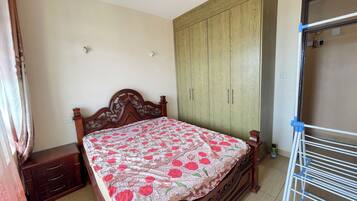 A bedroom with a wooden bed, a wardrobe, a nightstand, and a drying rack.