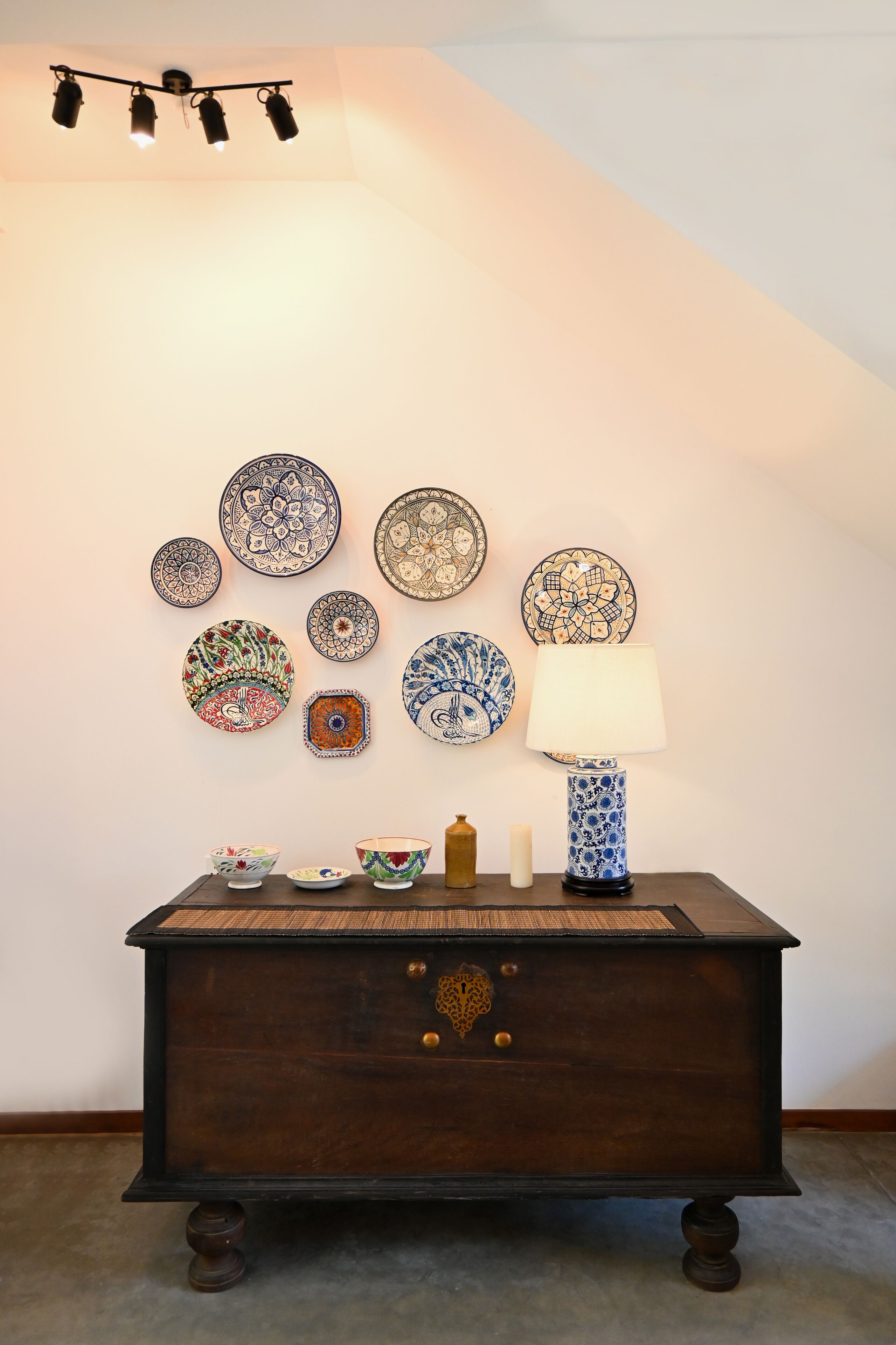 Un mur orné d’assiettes décoratives et une table avec une lampe et des bols.