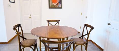 Un rincón comedor con una mesa redonda de madera, cuatro sillas de madera, un tapete estampado y un cuadro en la pared.
