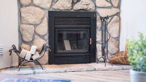 A stone fireplace with a black surround, a fire screen, and a metal log holder.