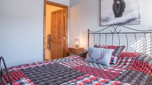 A bedroom with a checkered bedspread, a wooden door, a bedside table with a lamp, and a wall-mounted artwork of a bull.