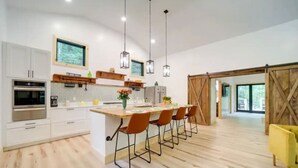 A modern kitchen with white cabinets, a large island with bar stools, pendant lighting, and a wooden floor. - 🔥 Fall Flash Sale –15% Off Waterfall deal Spacious 3 Bedroom Cabin Plus One Bedroom Beekeeper Cabin Waterfalls AWD or 4WD recommended (Hot Springs)