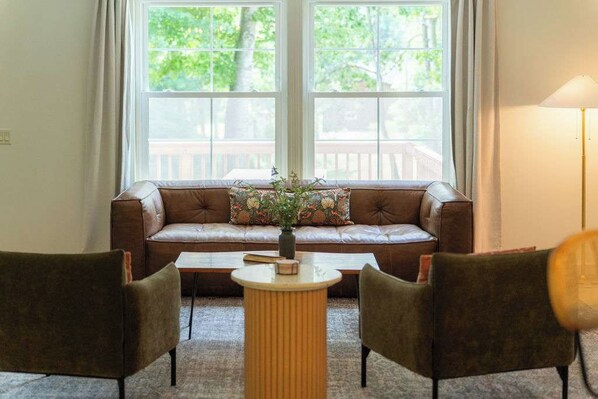 A room with a brown leather sofa, a small round table, and two chairs.