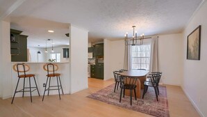 A dining area with a wooden table and chairs, a rug, and a chandelier.