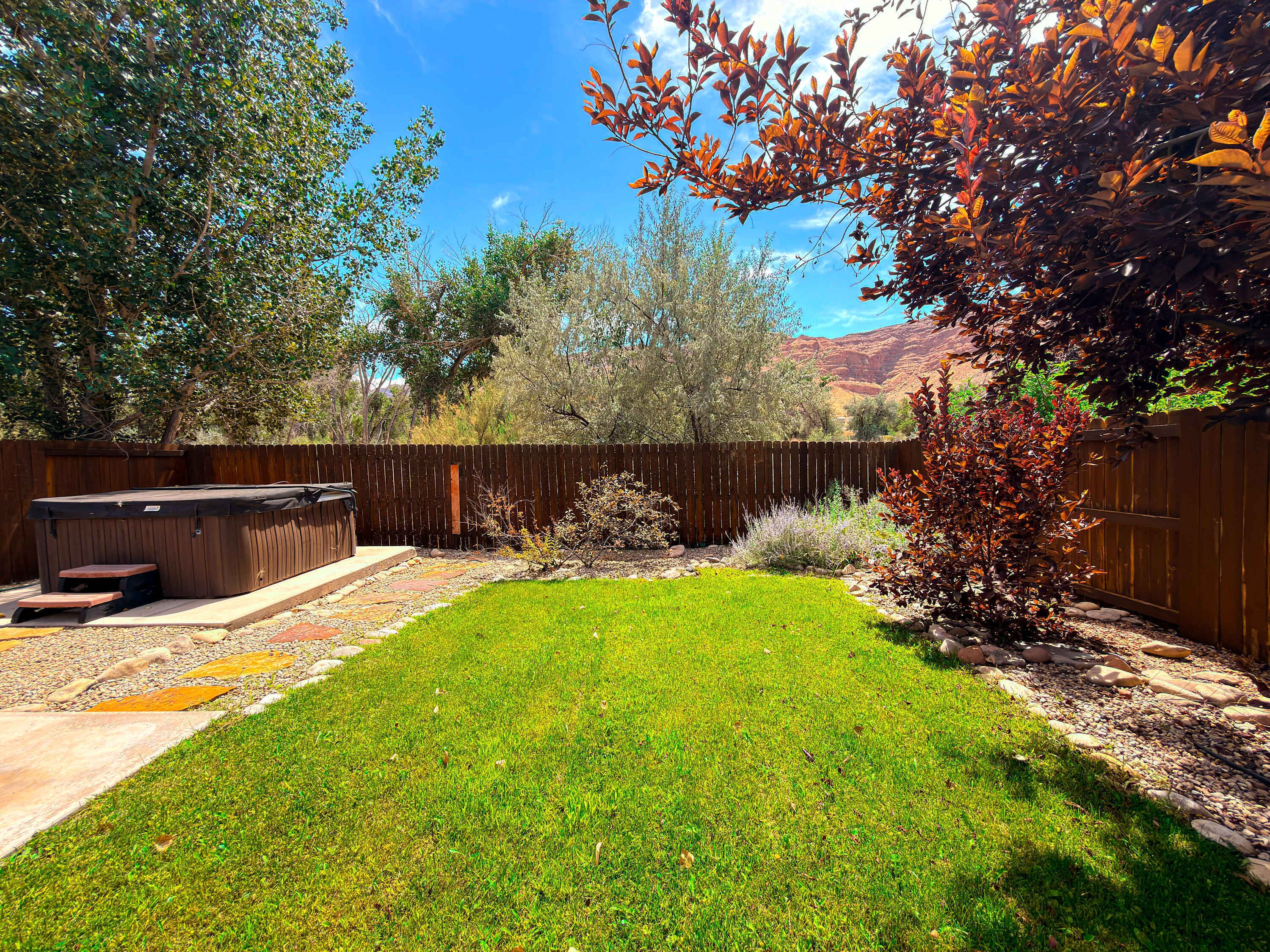 A backyard with a hot tub, a wooden fence, and a grassy lawn.