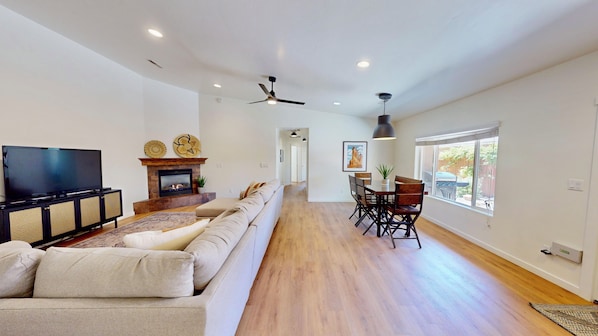 A spacious living room with a fireplace, a television, a sofa, and a dining area with chairs and a table.