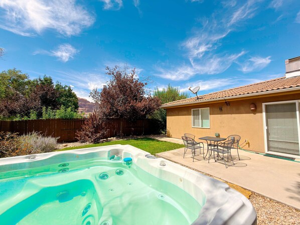 Un patio trasero con un jacuzzi, muebles de jardín y una casa con antena parabólica.