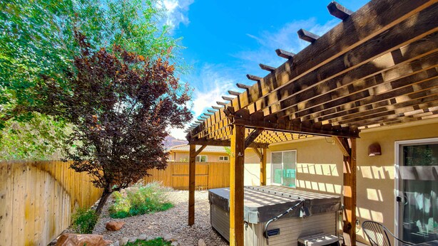 A backyard with a wooden pergola, a barbecue grill, and a patio area with chairs.