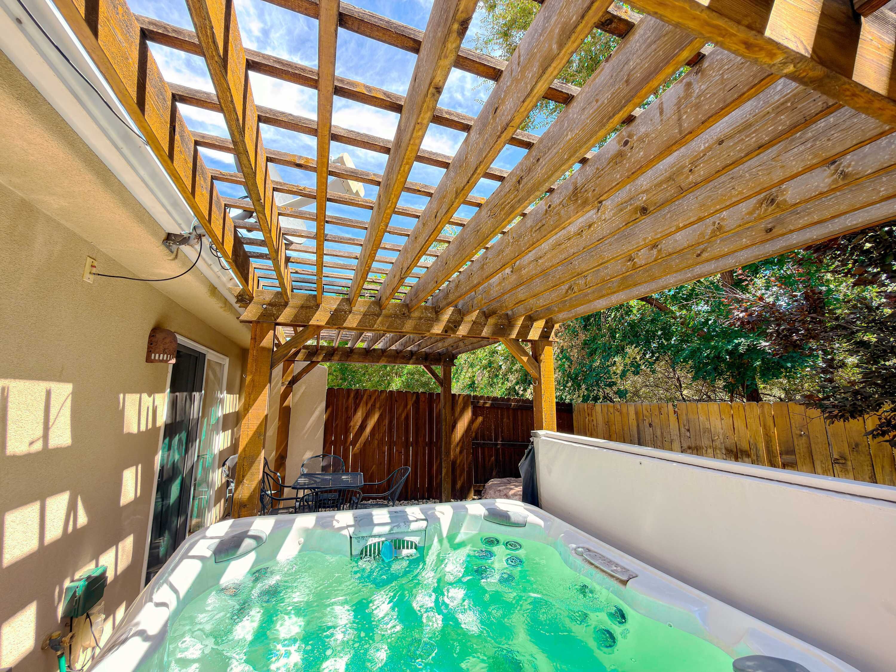 A hot tub under a wooden pergola with a wooden fence in the background.
