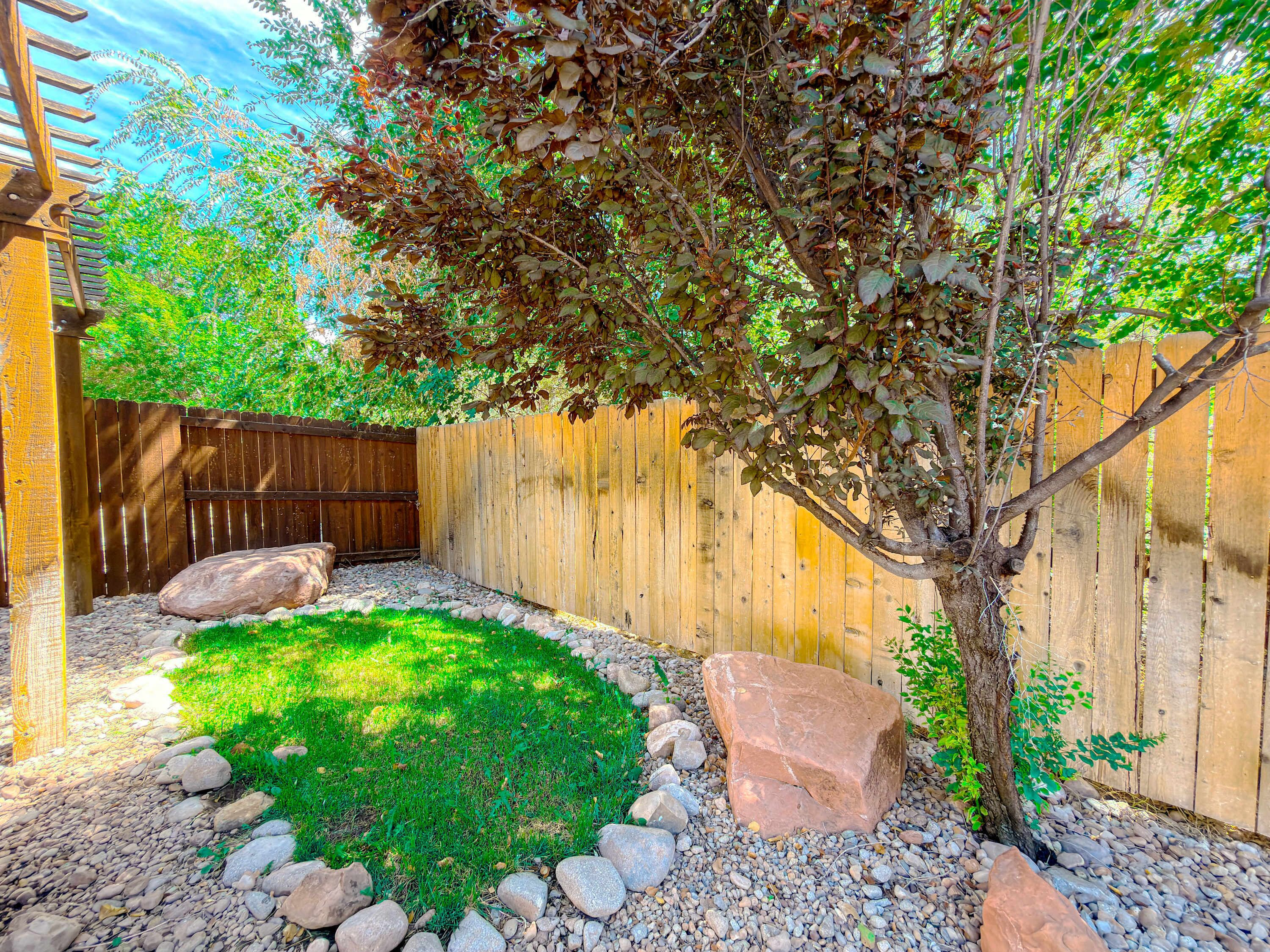 A fenced backyard with a tree, rocks, and a wooden fence.