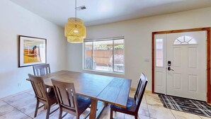 A dining area with a wooden table and chairs, a hanging light fixture, a door with a window, and a framed picture on the wall.