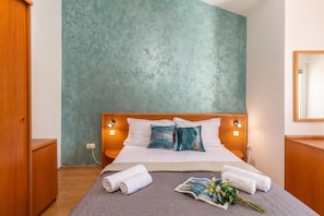 A hotel room with a bed, a bedside table, a nightstand, a wall-mounted lamp, and a mirror.