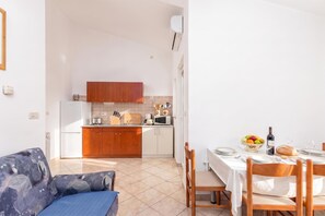 A modern kitchen with wooden cabinets, a dining area with a table set for two, and a patterned sofa. - Family Resort Santa Maria I Apartment 3, Stara Novalja, Croatia (Stara Novalja)