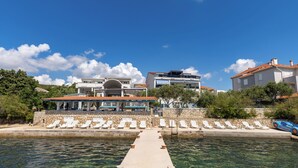Un hôtel situé au bord de l’eau, doté d’une piscine, de chaises longues et d’une jetée donnant accès à la mer.