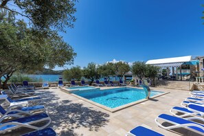 Uma área de piscina com espreguiçadeiras, céu claro e vista para o mar.