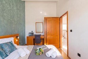 Une chambre d’hôtel avec un lit, un bureau, une chaise, une armoire et une salle de bain visible à travers une porte ouverte.