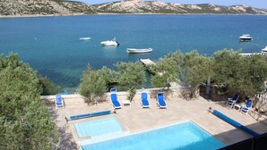 Un espace piscine avec des chaises longues et une vue sur la mer, où l’on peut apercevoir des bateaux.
