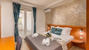 A hotel room with a bed, a table, a chair, a small bedside table, and an air conditioning unit. - Family Resort Santa Maria I Apartment 7, Stara Novalja, Croatia (Stara Novalja)