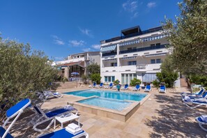 A hotel with a pool area, multiple lounge chairs, and a building with balconies. - Family Resort Santa Maria I Apartment 5, Stara Novalja, Croatia (Stara Novalja)
