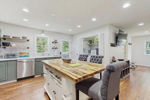 A modern kitchen with a wooden island, grey upholstered chairs, and built-in appliances.