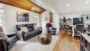 A spacious living area with a leather sofa, a round coffee table, and a dining area with chairs and a table. - Charming dog-friendly cottage near Blowing Rock with private hot tub, deck, BBQ (Blowing Rock)