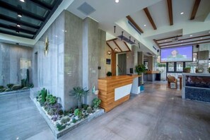 Un espace d’accueil comprenant un bureau en bois, un grand écran et un coin salon avec des chaises.