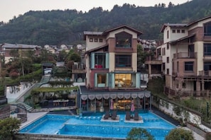 A multi-story building with a pool, balconies, and a view of the surrounding landscape. - Fangtingshu Hostel (Zhangjiajie)