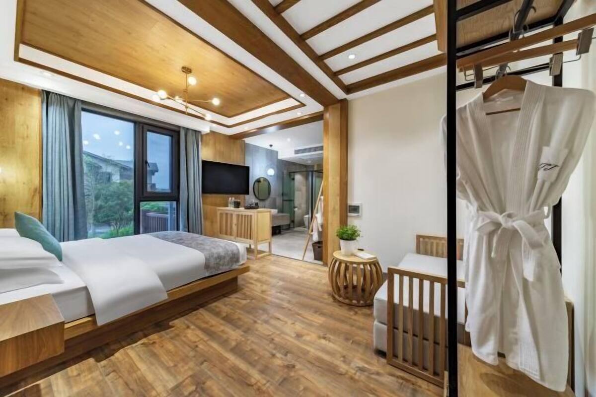 Un dormitorio moderno con techo de madera, una cama, un televisor y una bata colgada en un perchero.