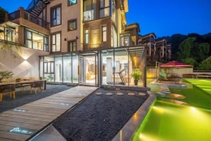 Un hotel moderno con un área exterior cubierta de vidrio, una terraza de madera y un jardín ajardinado.