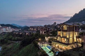 A multi-story building with a swimming pool, surrounded by a residential area with houses and hills in the background. - Fangtingshu Hostel (Zhangjiajie)