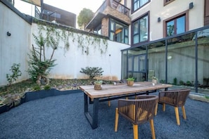 Un espacio de comedor al aire libre con una mesa y sillas, rodeado de grava y un muro bajo con plantas trepadoras.