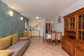 En kompakt opholdsstue med tekøkken, spiseplads og et indbygget træskab.
