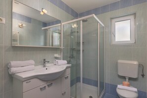 A bathroom with a glass-enclosed shower, a sink with a mirror, and a toilet.