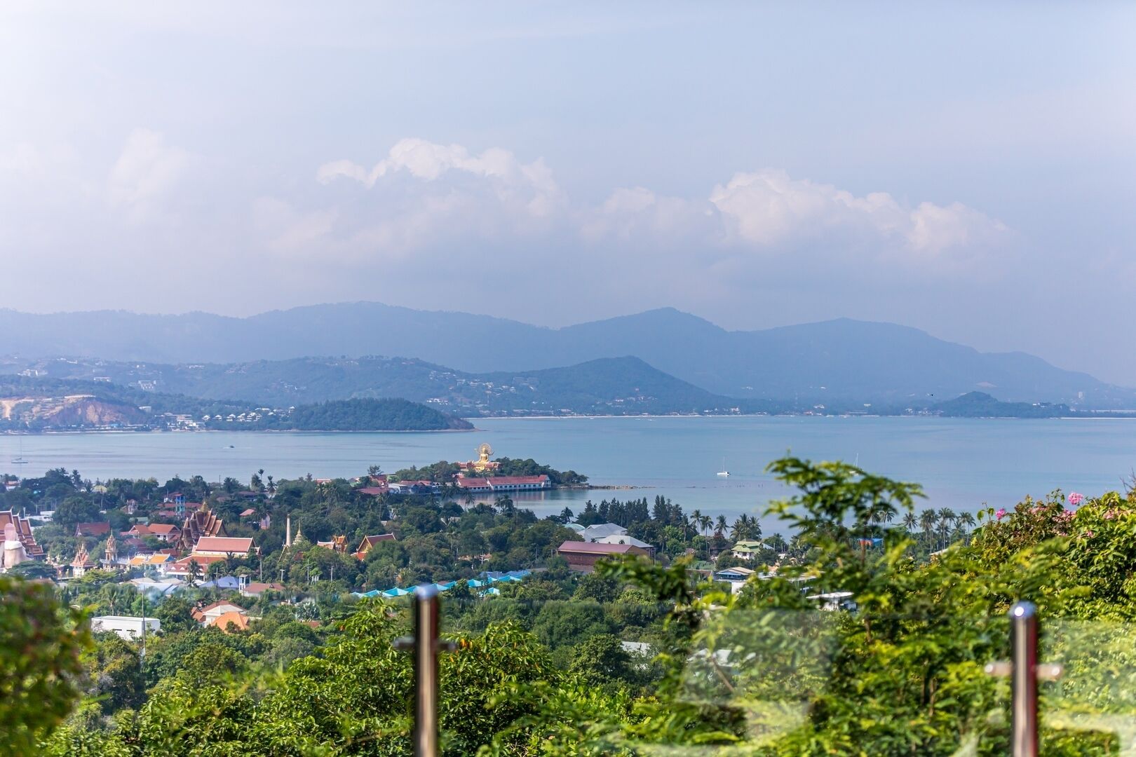 Una località costiera con un edificio imponente a cupola dorata, vegetazione rigogliosa e una vista limpida sul mare e sulle montagne in lontananza.