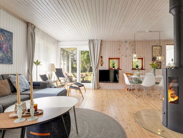Un salon moderne avec une cheminée, un téléviseur et un coin repas comprenant des chaises et une table.