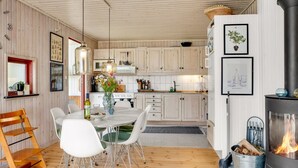 A modern kitchen with wooden cabinets, a dining area with a white table and chairs, and a fireplace.