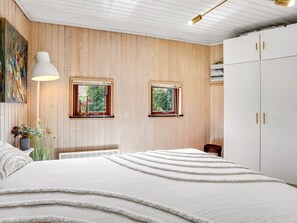Un dormitorio con cama, dos ventanas, un armario blanco y una lámpara.