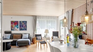 A modern living room with a sofa, chairs, a dining table, and artwork on the walls.