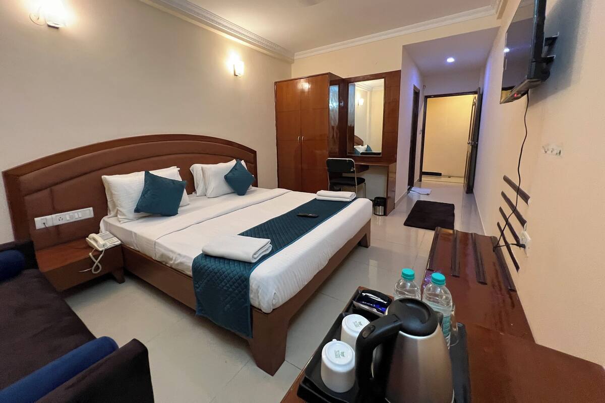 Habitación de hotel con una cama grande, mesita de noche, escritorio, silla y televisor montado en la pared.