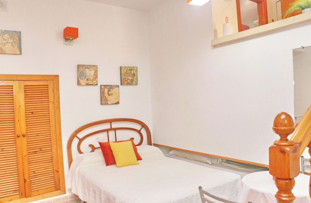 A bedroom with a bed, a wooden wardrobe, and a small shelf with decorative items.
