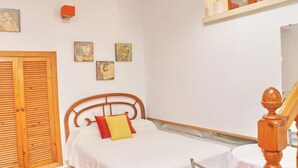A bedroom with a bed, a wooden wardrobe, and a small shelf with decorative items.