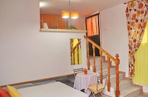 Une pièce comprenant un lit, une petite table avec une chaise, un escalier avec des rampes en bois et une fenêtre avec des rideaux.