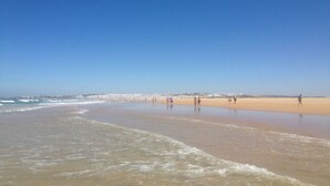 A beach with people walking and playing in the sand, and waves crashing onto the shore. - El Rinconcito de Pepa I,close to the beach (Conil de la Fra.)