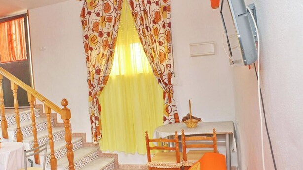A room with a staircase, a dining table with chairs, and a window with patterned curtains. - El Rinconcito de Pepa I,close to the beach (Conil de la Fra.)